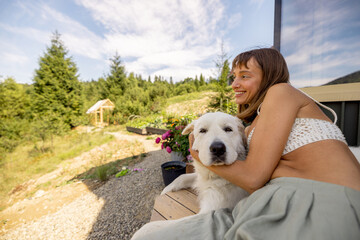 A woman sits on the porch, savoring a snack while her dog rests peacefully by her side. The lush...