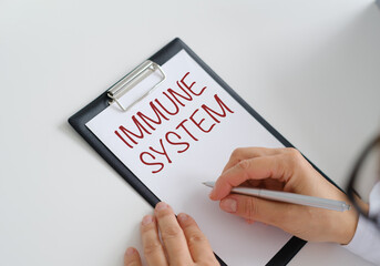 A person is writing the word Immune System on a clipboard