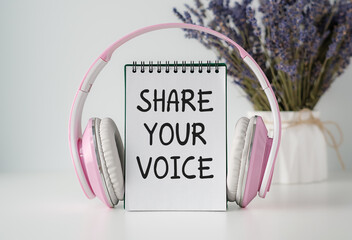 A pink and white notebook with a pink and white pair and text Share Your Voice of headphones on top...