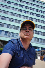 looking up at a mature man wearing a baseball cap and glasses in front of a multi-story building