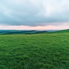 Obraz premium Rolling green hills under a cloudy sky, with a sunset peeking through.