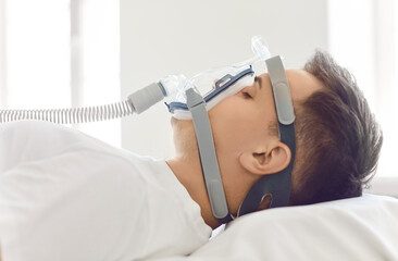 Close up side view of a male patient sleeping in a hospital bed with oxygen mask in white room....