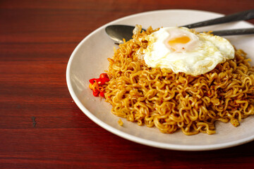 a fried instant noodle with egg toping and chili with wooden background