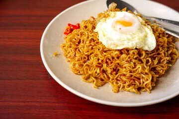 a fried instant noodle with egg toping and chili with wooden background