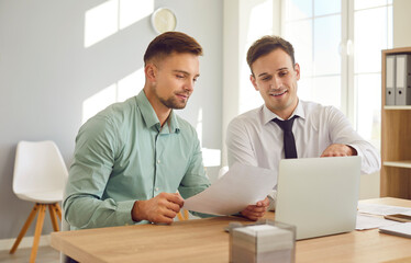 Two male colleagues are discussing documents at work meeting in bright office. Young Caucasian male...