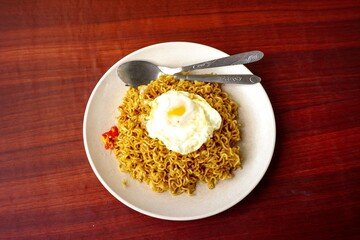 a fried instant noodle with egg toping and chili with wooden background
