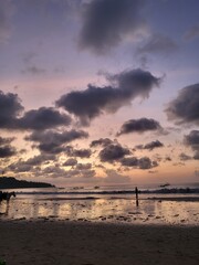 he evening sunset over the beach casts a beautiful glow with clouds in the sky and a soft...