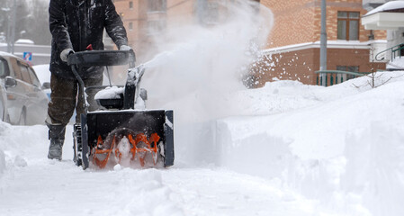 a man removes snow with a snow blower in the yard of a house