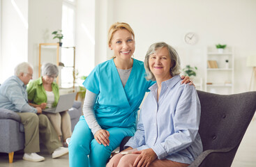 Smiling nurse sitting next to older woman, portrait. Friendly relations with nursing home staff....