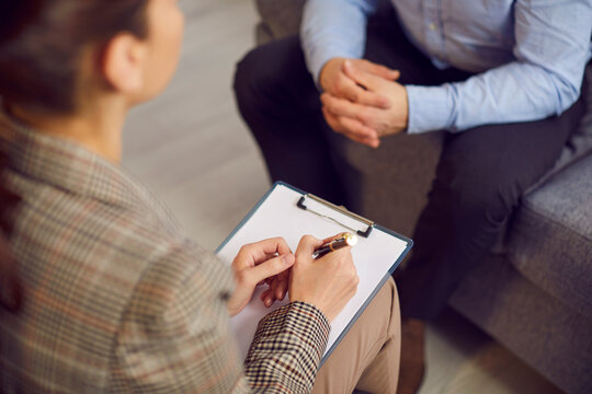 Woman therapist with a clipboard and a sheet of paper talking to a male patient during a psychotherapy session. Therapy, stress, mental health problems concept background