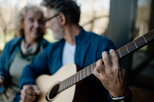 Man playing an accoustic guitar with his woman in background.