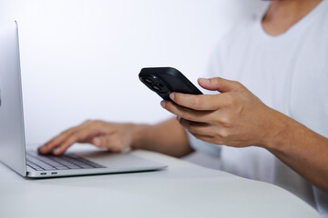 Middle-aged man in white shirt using laptop and smartphone on white background