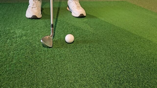 Practicing short game skills with a golf wedge and ball on indoor turf at a sports facility