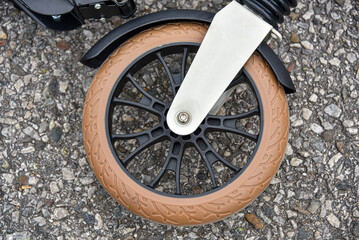 Front wheel of beige scooter on asphalt. Close-up.