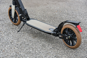 The deck of a folding scooter with beige wheels stands on the asphalt.