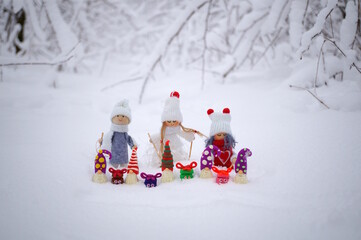 Toy angels in knitted hats and scarves. There are dwarfs and gifts nearby. Christmas decorations. Snow background.