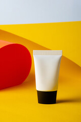 Plastic white tube for cream or lotion. Skin care or sunscreen cosmetic on orange and yellow background.