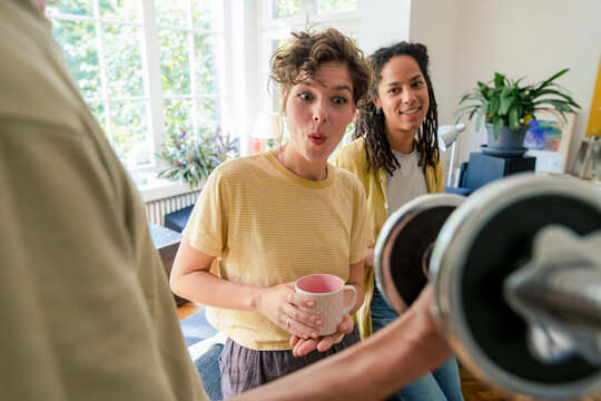Shocked young woman holding mug and standing with friend at home