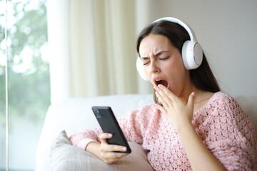 Bored woman yawning listening audio on phone