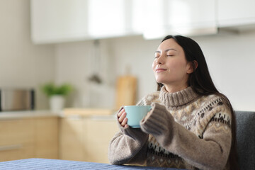 Asian woman breathing drinking coffee in the kitchen in winter