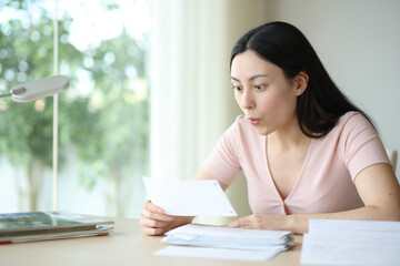 Surprised asian woman checking bill at home