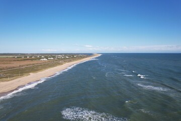 Aerial view of a sandy beach and ocean with houses in the background.