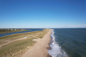 Aerial view of a coastal beach with ocean waves and grassy dunes.