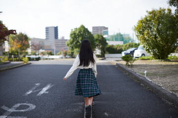 秋の昼の住宅街で散歩する小学生の女の子の姿