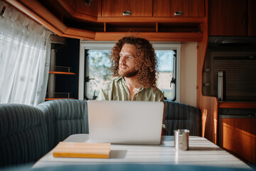 Young man working remotely from caravan. Man using camper as homeoffice, working on notebook.
