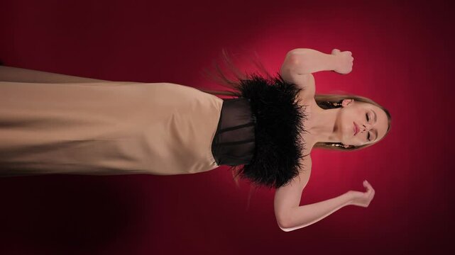 Beautiful young woman in black feather outfit posing on burgundy background