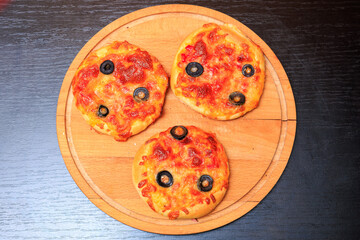 Three small pizzas with olives and cheese on a wooden board
