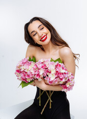 Woman smiling with pink hydrangeas. A young woman in black joyfully holds pink hydrangeas, smiling brightly in a studio.