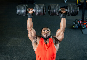 Weightlifting session at the gym. A muscular individual performs an overhead lift with heavy...