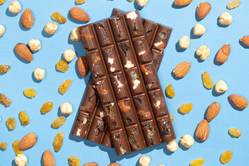 Nutty chocolate bars among scattered nuts and raisins on a blue background.