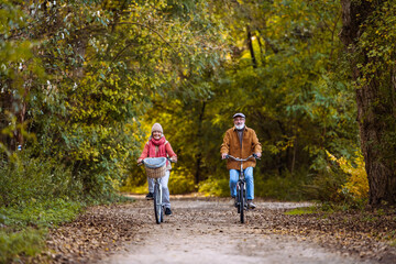 Obraz premium Beautiful elderly couple on bike ride in the forest. Seniors in love cycling through autumn nature, enjoying a peaceful moment.