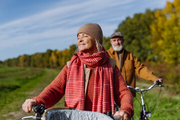 Lovely elderly couple on a walk in the forest, pushing their bikes side by side. Seniors in love on...