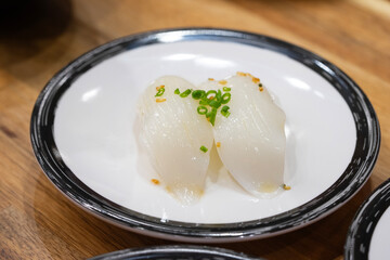 A white plate with a squid sushi piece, nigiri sashimi, on a bed of rice.