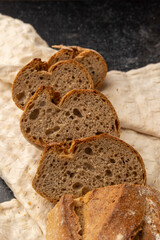 Artisan sliced bread in rustic style, arranged neatly on a dark, textured surface that adds a contrast highlighting the bread's crust and crumb textures vividly.