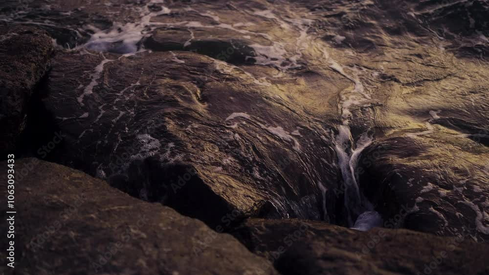 Poster slow motion view of waves breaking on rocks with reflective dusk light, creating a serene coastal sc