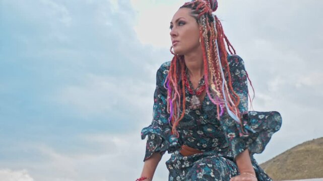 Pretty woman in boho style with dreadlocks against a cloudy sky