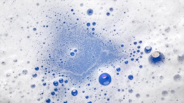 Foam background. Liquid soap bubbles, Froth bubbles popping backdrop. Soap foam structure over blue. Soap sud macro, close-up. Clean, cleaning, washing, laundry. Top view, high speed video from above.
