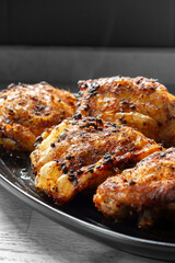 Fried chicken with hot thai bbq seasoning on a black stoneware dish. On wooden background