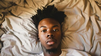 Man lying in bed with wide-open eyes, showing deep concern and fatigue, unable to sleep in dimly lit room with soft glow from nightstand lamp.