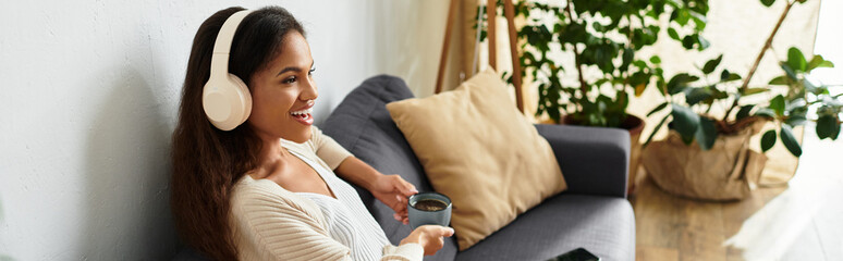 A cheerful woman immersed in music while sipping from her mug in a stylish living area.
