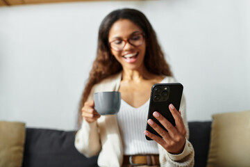 A smiling woman sips coffee and engages with her smartphone in a relaxed setting.