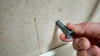 A hand inserts a wall anchor into a drilled tile, illustrating DIY home repair and renovation...