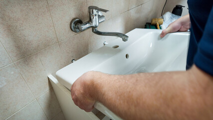 A person installing a white bathroom sink symbolizes home improvement and plumbing repairs