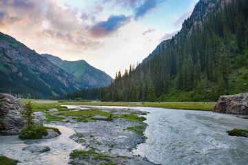 Idyllic summer landscape with hiking trail in the mountains with beautiful fresh green mountain pastures, river with reflection and forest.