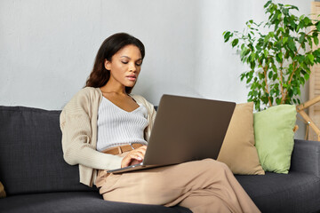 A beautiful woman engages with her laptop while seated comfortably in a soothing space.