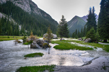 Idyllic summer landscape with hiking trail in the mountains with beautiful fresh green mountain pastures, river with reflection and forest.